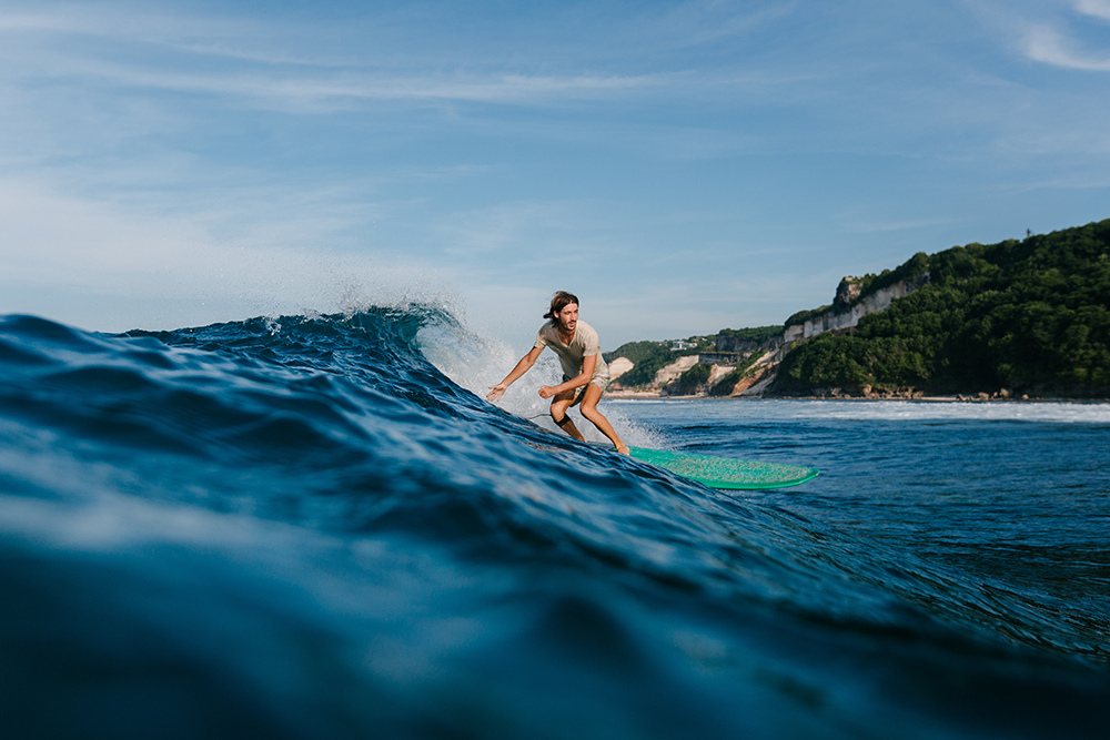 side view of man in wet t-shirt riding blue ocean waves on surfboard
